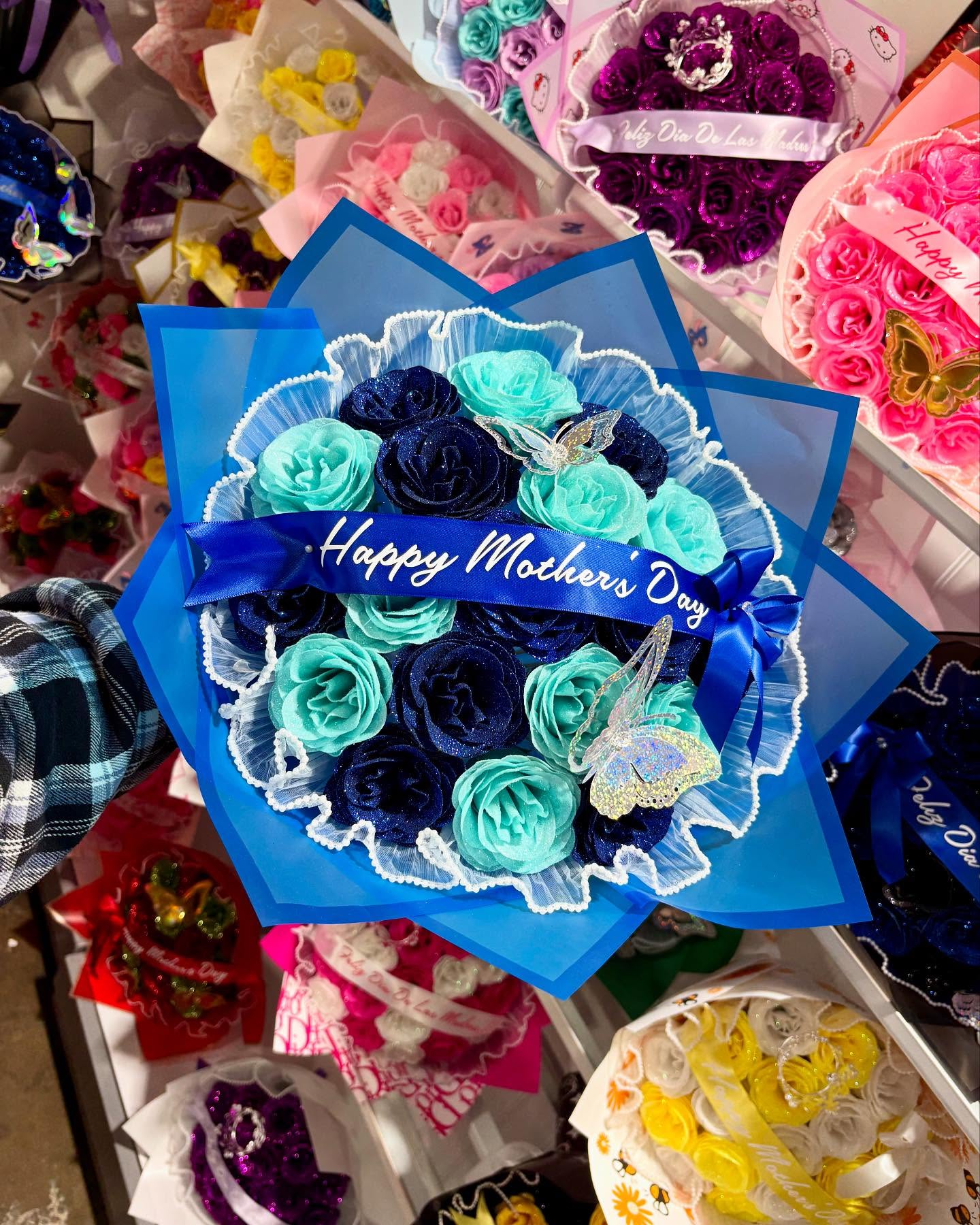 Blue and turquoise rose bouquet with butterfly accents and a “Happy Mother’s Day” ribbon