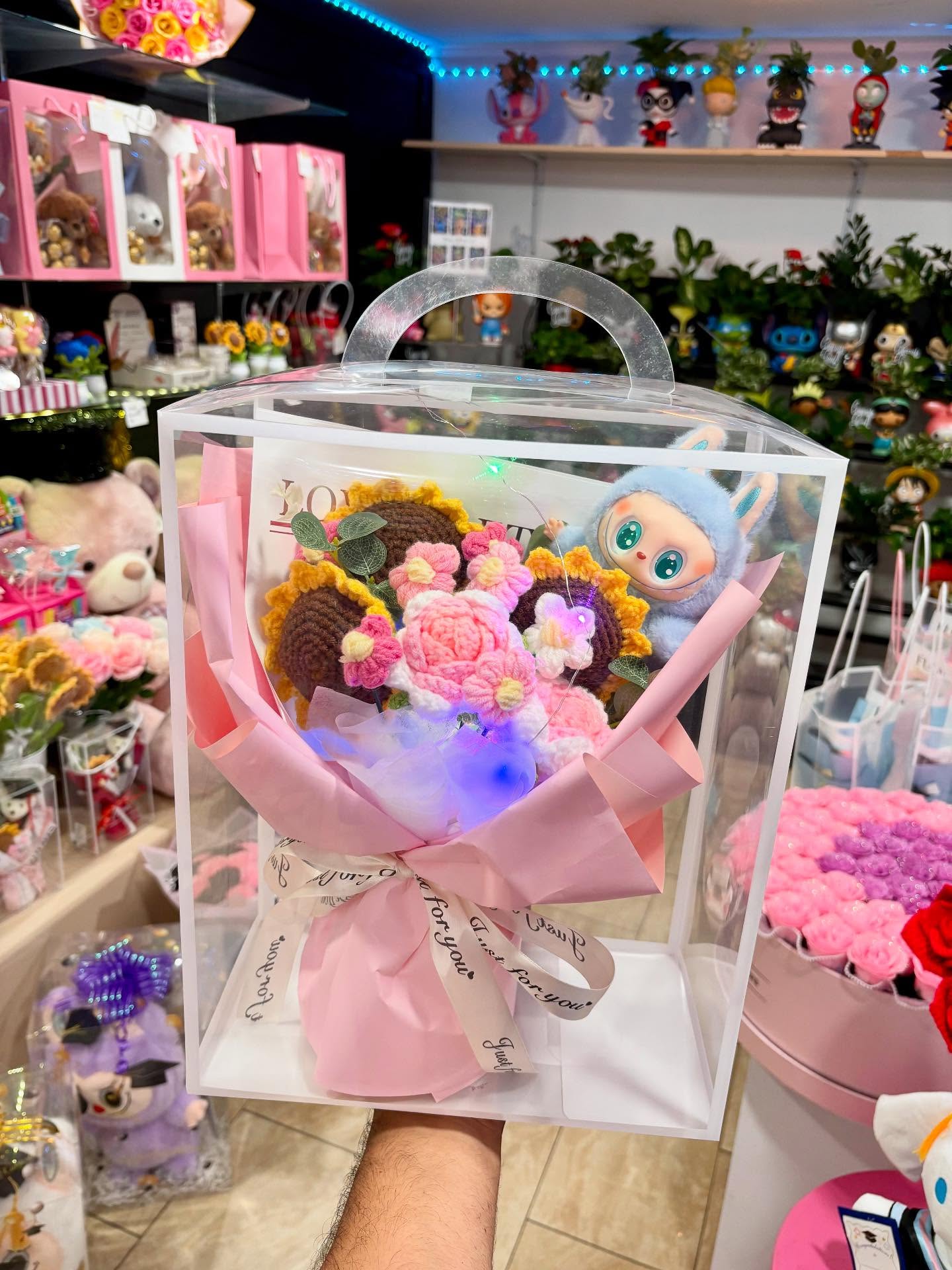 Crochet flower bouquet with a plush character in a clear gift box at The Hidden Gift Store