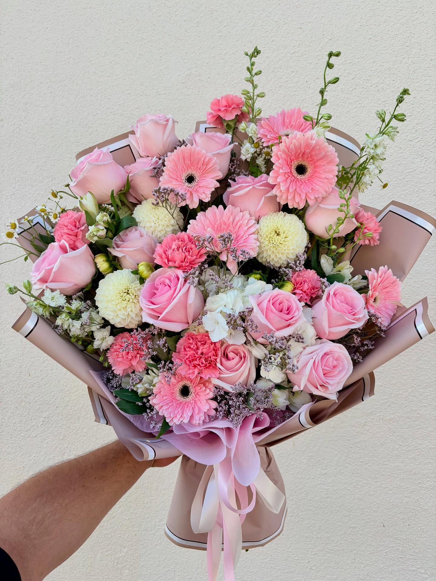 Pink floral bouquet with roses, gerbera daisies, carnations, white flowers, greenery, and elegant pink wrapping from The Hidden Gift Store