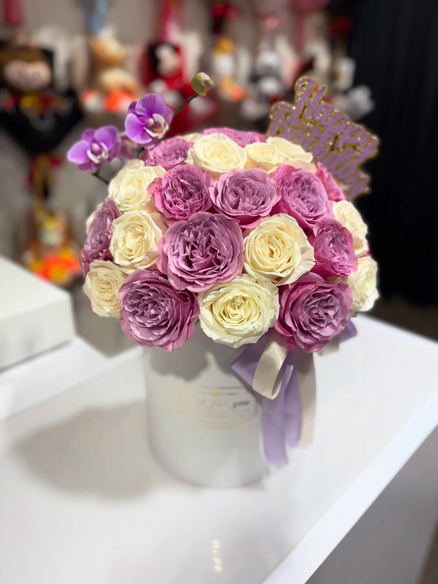 Birthday flower arrangement with lavender and white roses, purple orchids, and Happy Birthday decoration