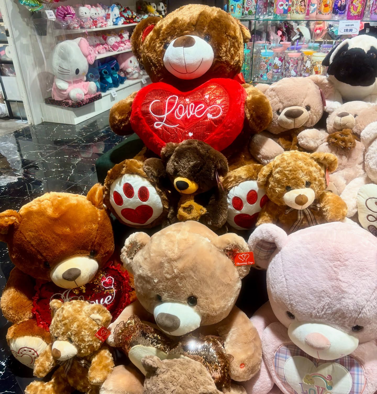 Gift shop display featuring teddy bears and plush animals, including large bears holding red love hearts