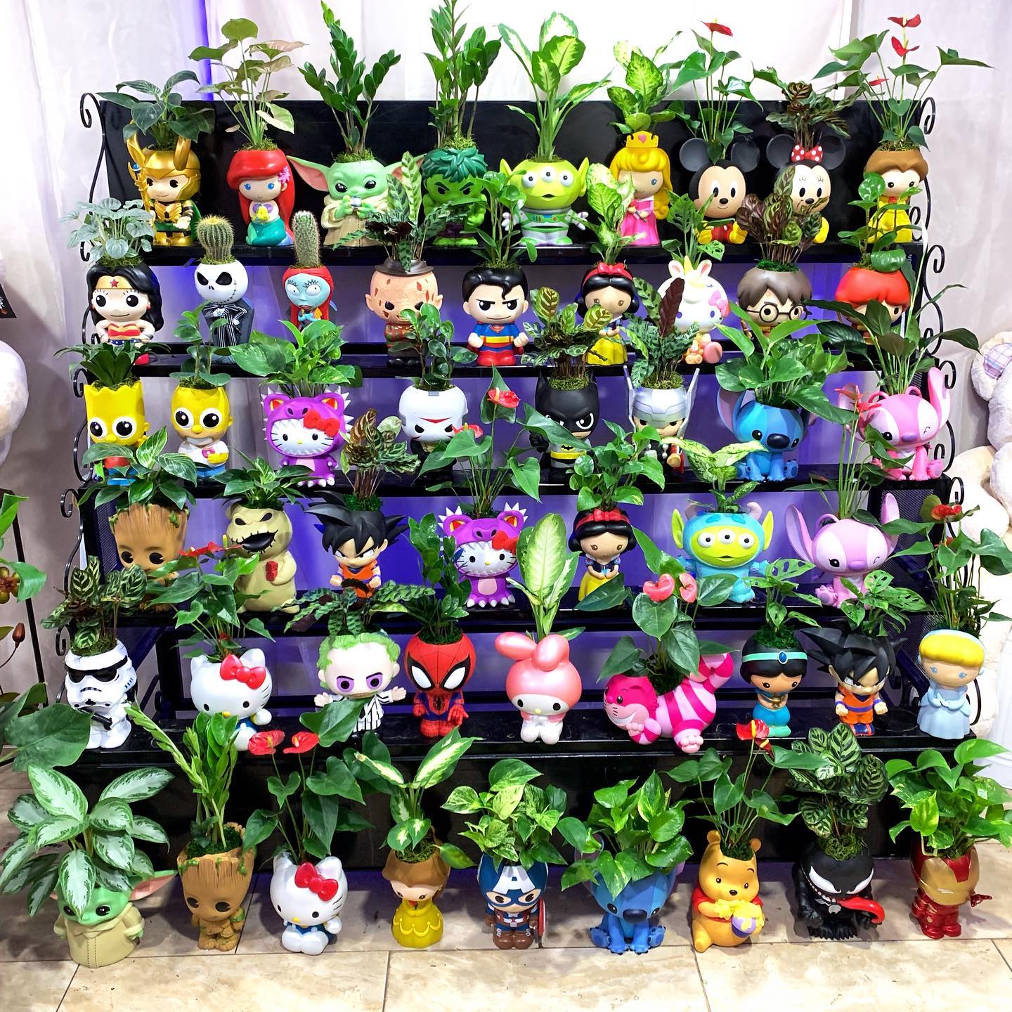 A large tiered display stand filled with dozens of small indoor houseplants potted in pop culture character planters, featuring recognizable figures from Disney, Marvel, Star Wars, and Sanrio.