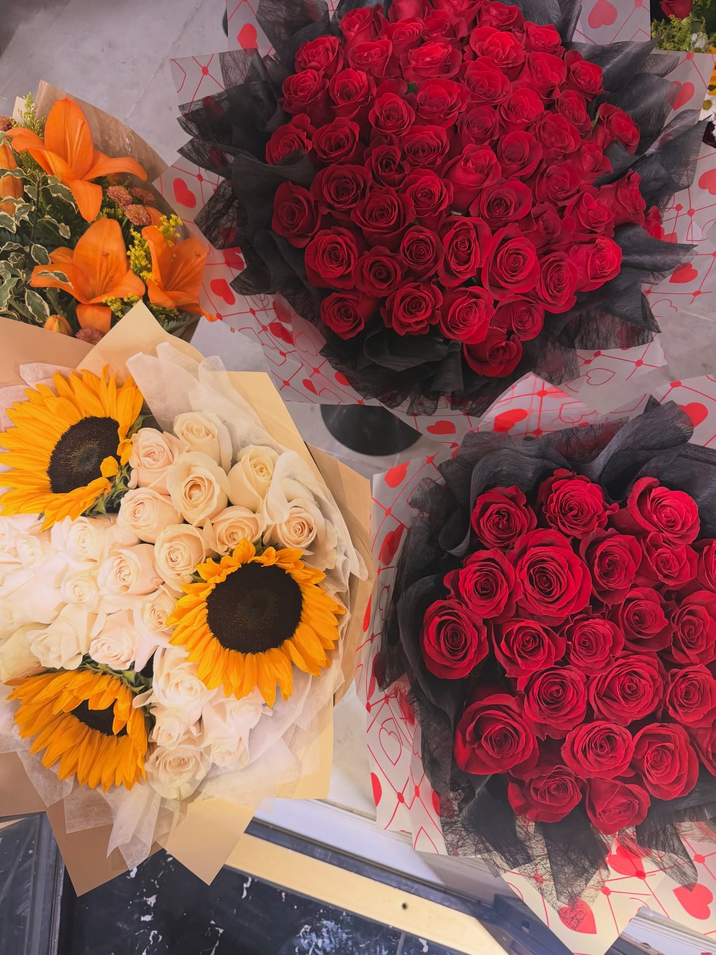 Red rose bouquets and a sunflower bouquet with cream roses displayed at a flower shop