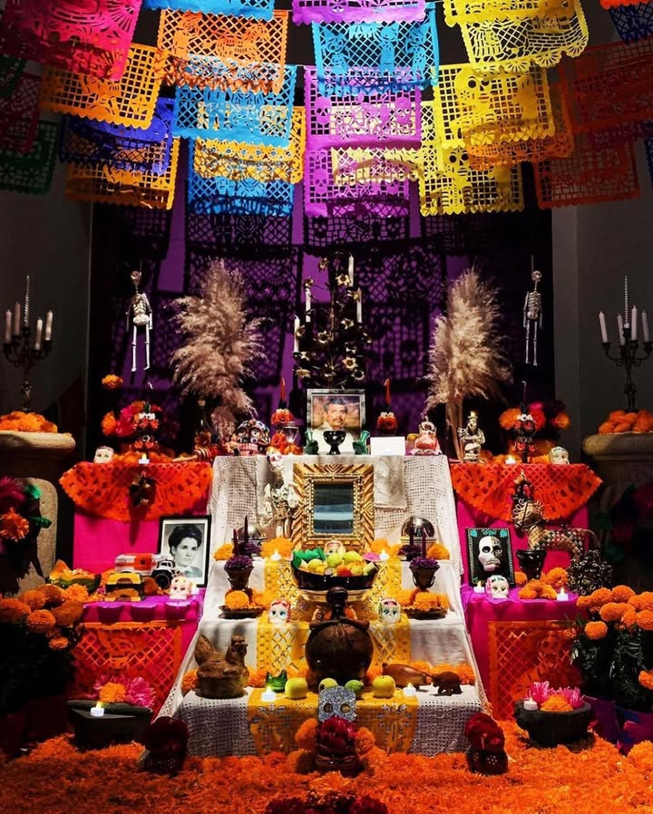 Traditional Día de los Muertos altar decorated with marigold flowers, papel picado, candles, photos, and colorful offerings
