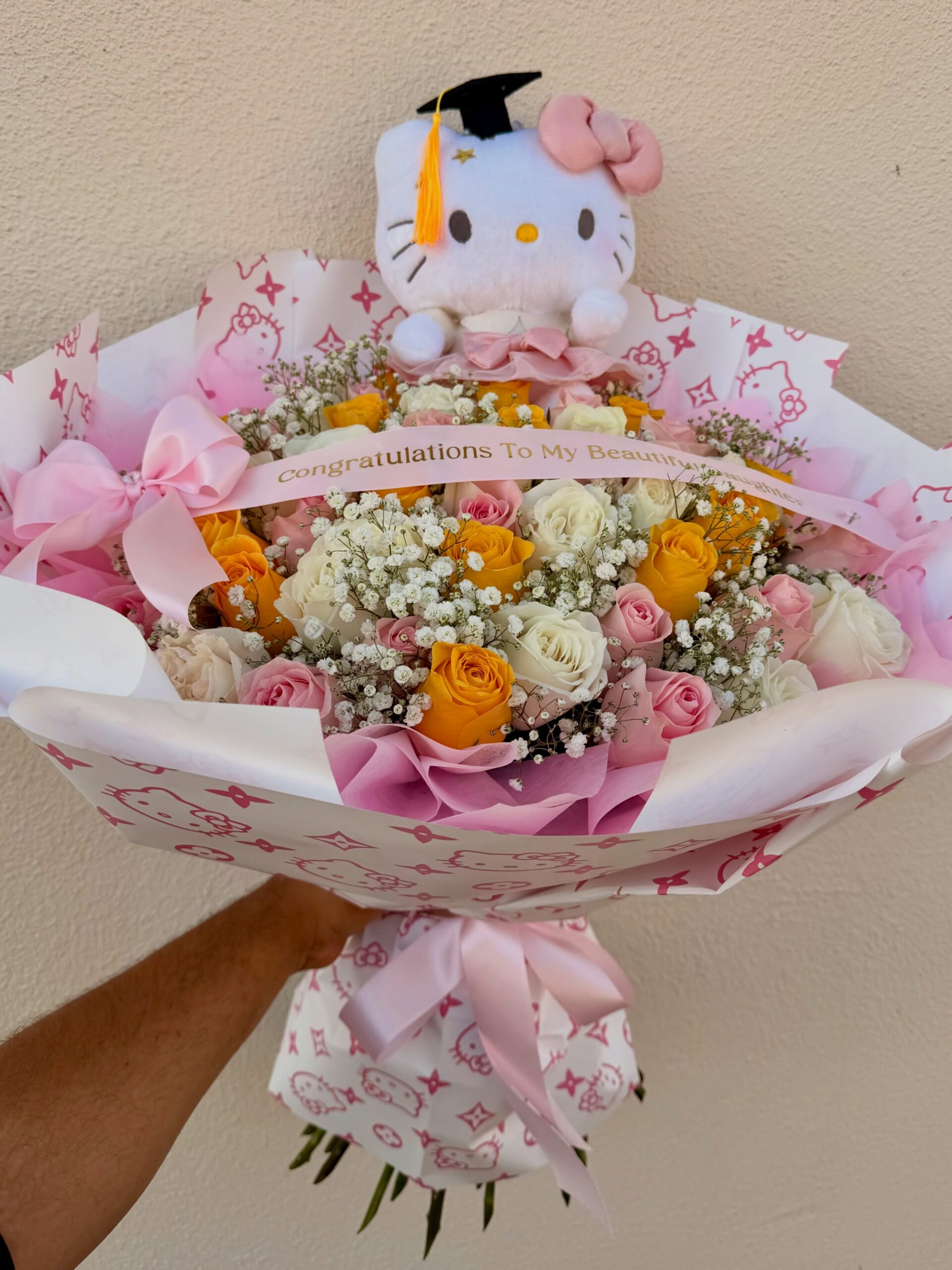 Graduation flower bouquet with pink, white, and yellow roses, baby’s breath, and a graduation-themed plush gift