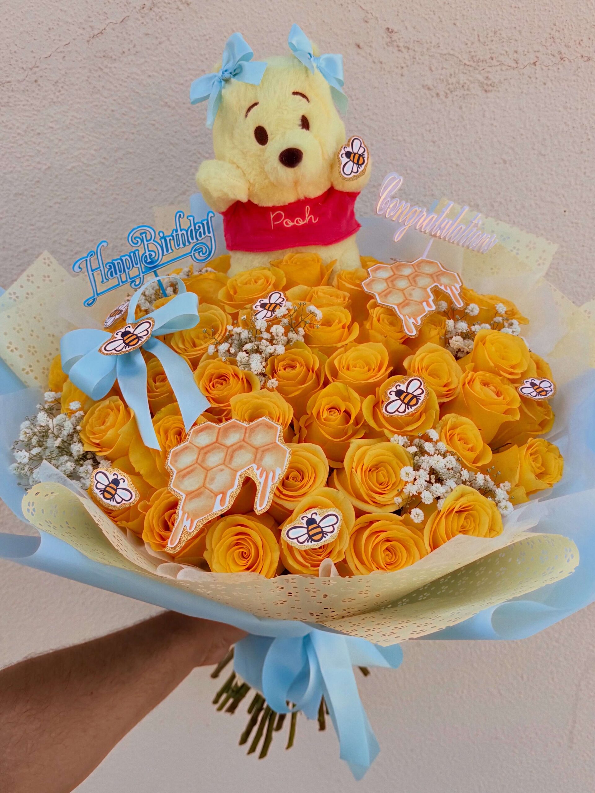 Yellow rose bouquet with blue ribbon, bee decorations, and Winnie the Pooh birthday plush